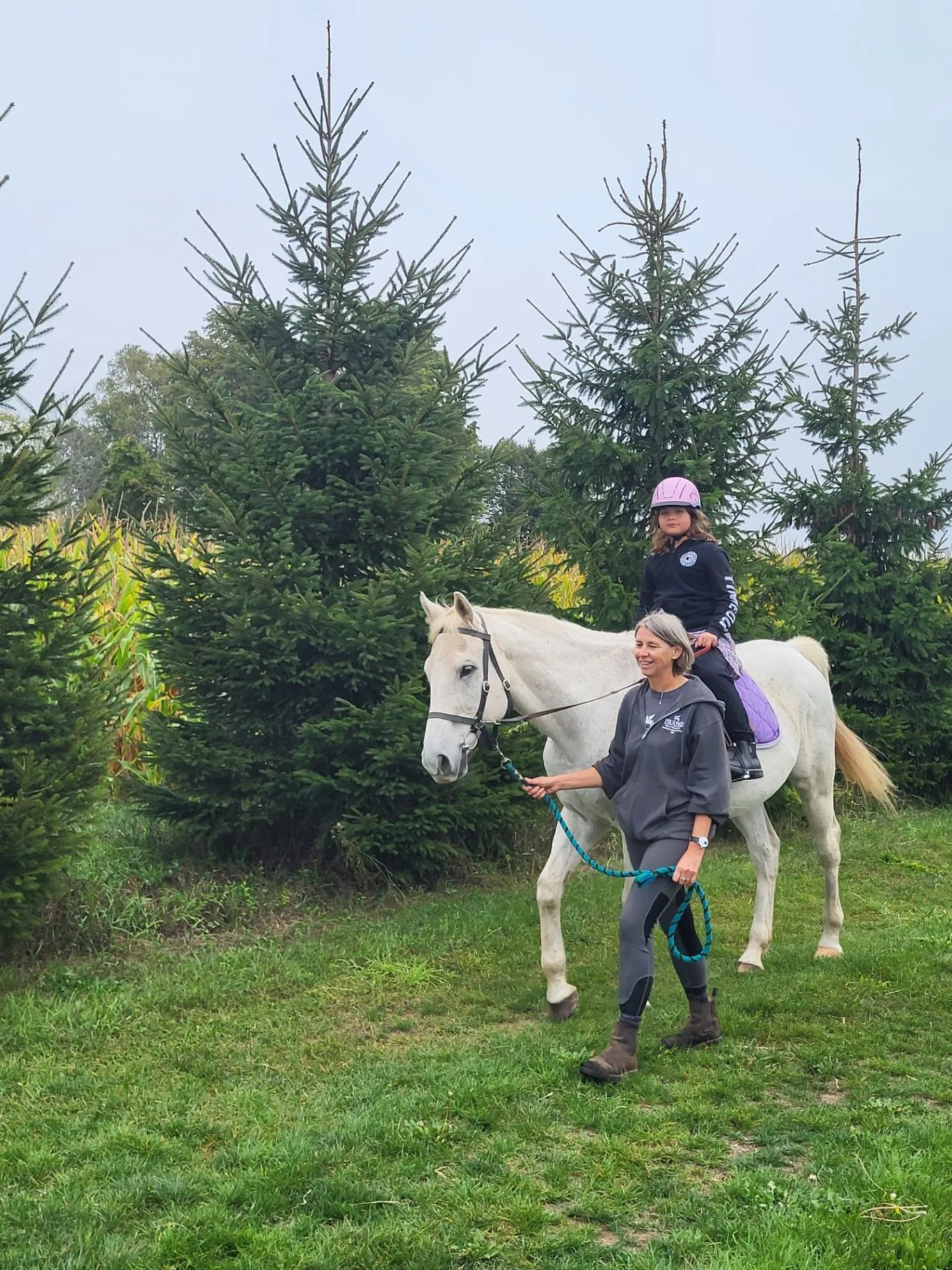 A young rider on a white horse being led along a trail by a staff member
