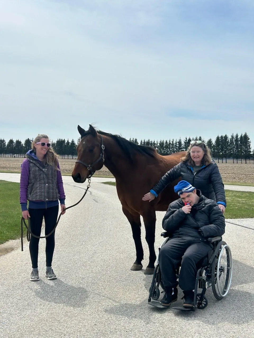 A young person in a wheelchair meeting a horse with two staff members at an arena